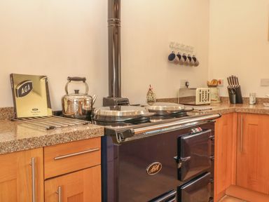 A kitchen corner with a stove kettle mugs on hooks and a knife block at Back Of Beyond in St Ives