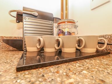 A kitchen countertop with a coffee machine four cups and a jar of coffee capsules at Back Of Beyond in St Ives