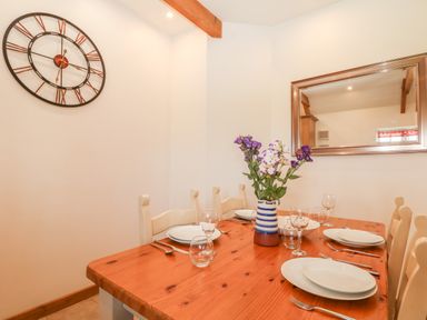 A dining room with a wooden table set with plates glasses and cutlery and flowers in a vase on the table at Back Of Beyond in St Ives