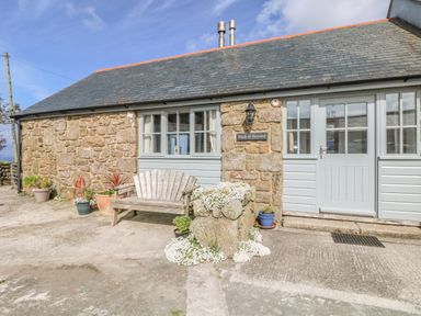 A stone and wood house exterior with a bench and flower pots at Back Of Beyond in St Ives