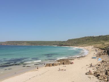 A sandy beach with people near the water and rocky hills in the background at Back Of Beyond in St Ives