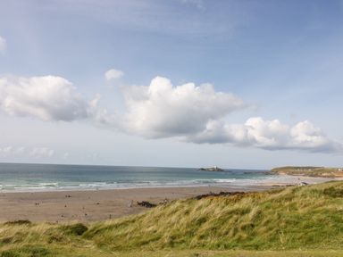 A beach with people on the sand and grassy dunes in the foreground with an ocean and cloudy sky at Angarrack Farmhouse in Hayle