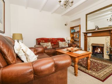 A living room with brown leather sofas a wooden coffee table a lit fireplace a patterned rug and a wooden bookshelf at Angarrack Farmhouse in Hayle