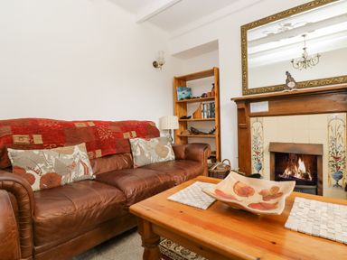 A living room with a brown leather sofa red and beige cushions wooden coffee table and a fireplace with a mirror at Angarrack Farmhouse in Hayle