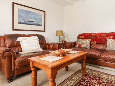 A living room with two brown leather sofas a wooden coffee table a lamp and a framed painting on the wall at Angarrack Farmhouse in Hayle
