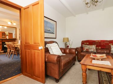 A living room with brown leather sofas a wooden coffee table and a door opening to a dining room at Angarrack Farmhouse in Hayle