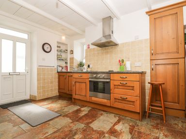 A kitchen with wooden cabinets a stainless steel oven a stove and extractor fan a stool and a door at Angarrack Farmhouse in Hayle