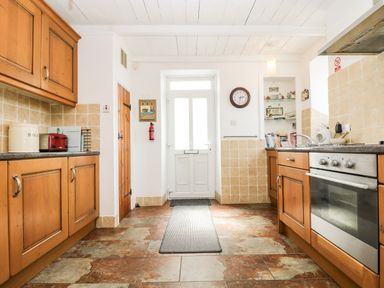 A kitchen with wooden cabinets a oven a toaster and a door at Angarrack Farmhouse in Hayle