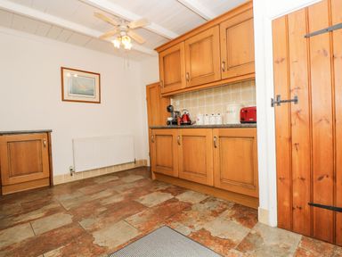 A kitchen with wooden cabinets tiled floor ceiling fan and a wooden door at Angarrack Farmhouse in Hayle