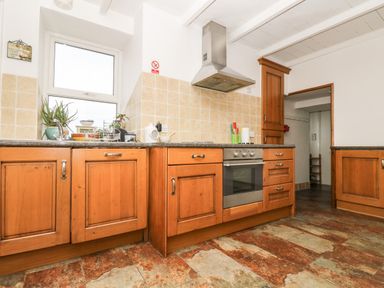 A kitchen with wooden cabinets a stainless steel oven and stove a window and tiled floor at Angarrack Farmhouse in Hayle