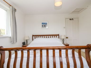 A bedroom with a wooden bed frame white bedding two bedside tables with lamps a window with striped curtains and a door at Angarrack Farmhouse in Hayle