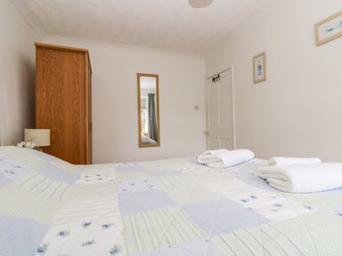 A bedroom with a bed covered in a quilt with folded towels a wooden wardrobe a wall mirror and framed pictures at Angarrack Farmhouse in Hayle