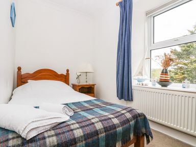 A small bedroom with a single wooden bed white bedding a plaid blanket and a bedside table with a lamp and flower at Angarrack Farmhouse in Hayle