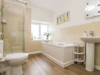 A bathroom with a toilet shower bathtub sink and a small corner shelf with decorations at Angarrack Farmhouse in Hayle