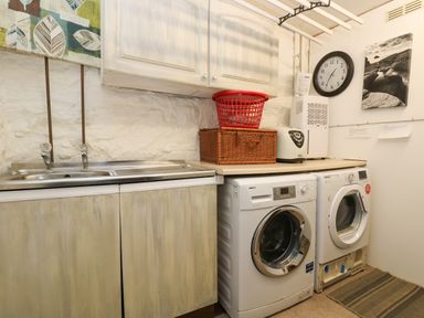 A utility room with a washer dryer sink cabinets a clock and laundry baskets at Angarrack Farmhouse in Hayle