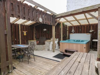 An outdoor covered patio area with a hot tub a dining table with four chairs and a wooden bench at Angarrack Farmhouse in Hayle