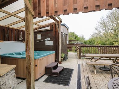 An outdoor covered hot tub next to a wooden picnic table and chairs on a deck surrounded by wooden fencing at Angarrack Farmhouse in Hayle
