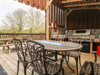 An outdoor covered deck with a metal table and chairs a barbecue grill and a wooden picnic table at Angarrack Farmhouse in Hayle