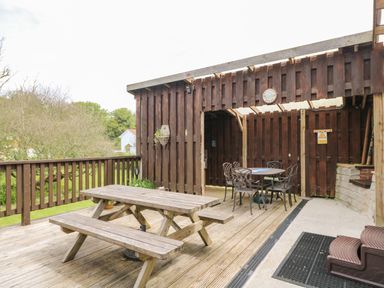 A wooden outdoor deck with a picnic table and a covered seating area with metal chairs at Angarrack Farmhouse in Hayle
