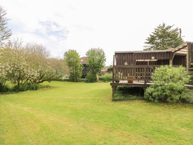 A garden with grass trees and a wooden deck with a pergola at Angarrack Farmhouse in Hayle
