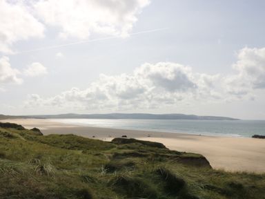 A sandy beach with grassy dunes in the foreground and hills in the background at Angarrack Farmhouse in Hayle