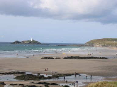 A beach with people on the sand and in the water with a lighthouse on an island in the distance at Angarrack Farmhouse in Hayle