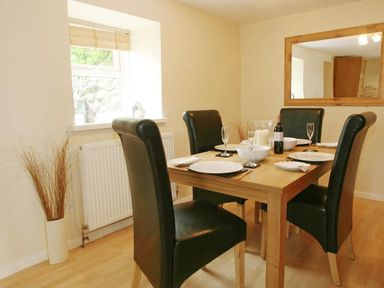 A dining room with a wooden table set for four with black chairs and a large wall mirror at Godrevy Cottage in Hayle