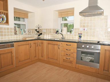 A kitchen with wooden cabinets tiled backsplash and stainless steel appliances at Godrevy Cottage in Hayle