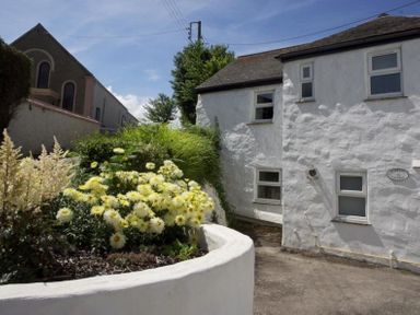 A white stone building with multiple windows next to a garden with yellow flowers at Godrevy Cottage in Hayle