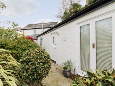 The exterior side view of a white building with plants and shrubs along a concrete pathway at Godrevy Barn in Hayle
