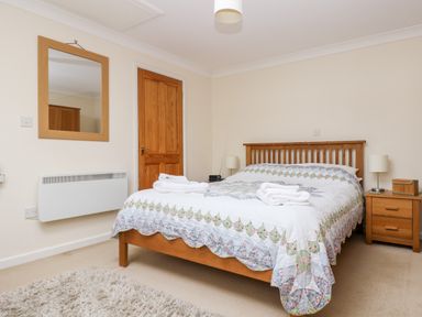A bedroom with a double bed covered with a quilt and two folded towels on top beside wooden bedside tables with lamps and a wall mirror at Godrevy Barn in Hayle