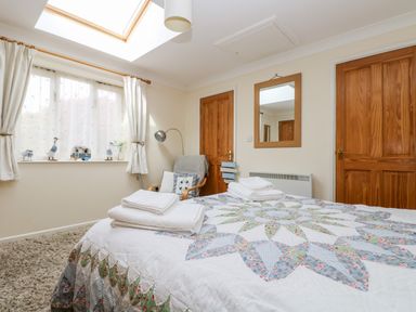 A bedroom with a bed with patterned quilt and folded towels two wooden doors a chair and a window with curtains at Godrevy Barn in Hayle