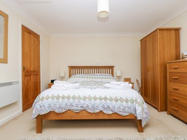 A bedroom with a wooden bed frame blankets and towels two bedside tables lamps a wardrobe and a chest of drawers at Godrevy Barn in Hayle