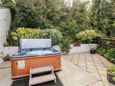 An outdoor patio area with a hot tub and steps surrounded by plants and trees at Godrevy Barn in Hayle