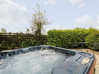 An outdoor hot tub with bubbling water near a wooden fence a shrub and metal table with chairs at Godrevy Barn in Hayle