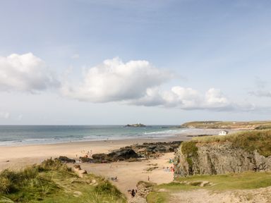 A sandy beach with people near rocks and grassy cliffs under a partly cloudy sky at Godrevy Barn in Hayle