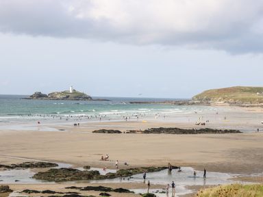 A beach with people on the sand and in the water with a lighthouse on an island in the distance at Godrevy Barn in Hayle