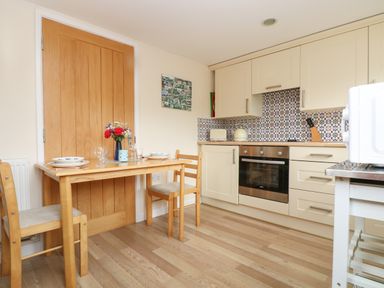 A kitchen with a wooden table set for two and beige cabinets with tiled backsplash at Little Hamlin in Rilla Mill Nr Callington