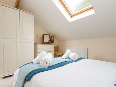 A bedroom with a bed with rolled white towels a wardrobe a chest of drawers a chair and a skylight window at Little Hamlin in Rilla Mill Nr Callington