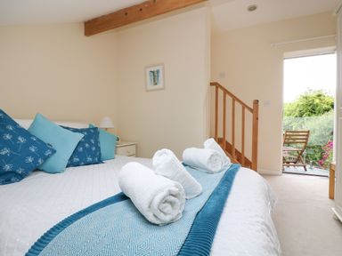 A bedroom with a bed with blue and white pillows and rolled towels next to a staircase and a balcony at Little Hamlin Rilla Mill Nr Callington