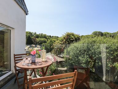 A balcony with wooden table and chairs glass railing flowers in vase and greenery outside at Little Hamlin in Rilla Mill Nr Callington