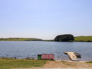A lake with a wooden dock and a small boat near green fields and trees at Little Hamlin in Rilla Mill Nr Callington