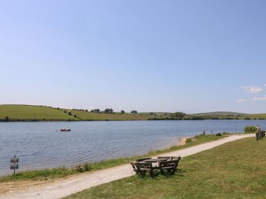 A lakeside with a wooden round bench and a path along the water at Little Hamlin in Rilla Mill Nr Callington