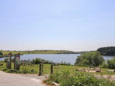 A lakeside grassy area with a playground and picnic benches at Little Hamlin in Rilla Mill Nr Callington
