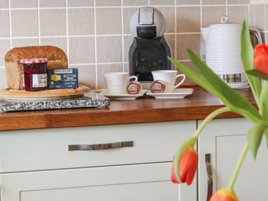 A kitchen countertop with a coffee machine two cups a loaf of bread butter and jam at Honeysuckle Cottage in Helston