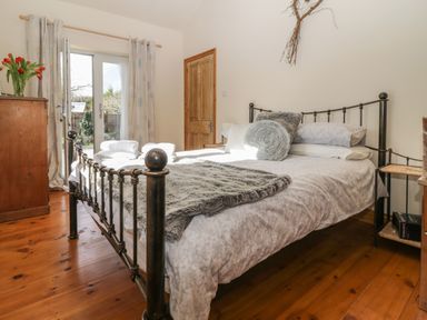 A bedroom with a metal bed frame wooden floor chest of drawers and glass doors leading outside at Honeysuckle Cottage in Helston