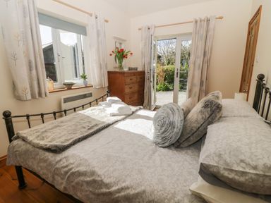 A bedroom with a bed pillows and towels near a window and a dresser with flowers at Honeysuckle Cottage in Helston