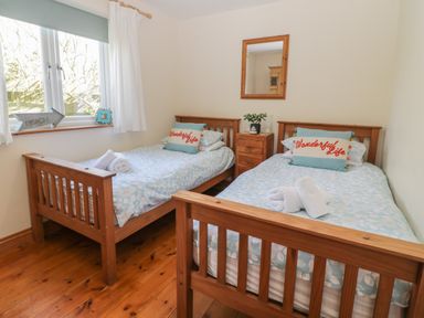 A bedroom with two single wooden beds with blue floral bedding and pillows that say Wonderful Life at Honeysuckle Cottage in Helston