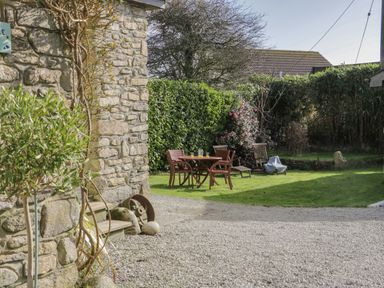 A garden with wooden chairs and a table with drinks near a stone building at Honeysuckle Cottage in Helston