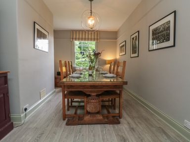 A dining room with a wooden table and six chairs set with plates and glasses at Penwarne Lodge in Mawnan Smith